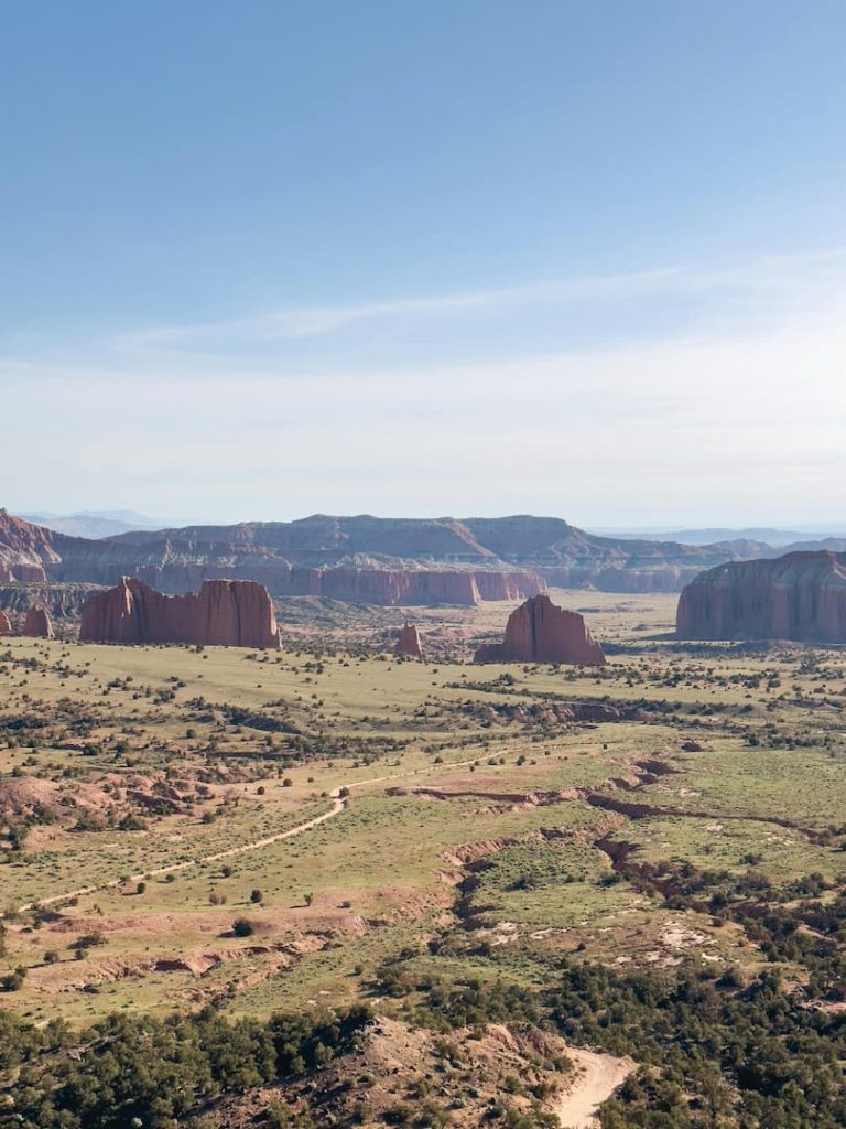 Photo de la valley à Capitole Reef National Park, prise depuis els hauteurs montrant à la fois les roches rouge et les plaines vertes, avec la route serpentant au centre