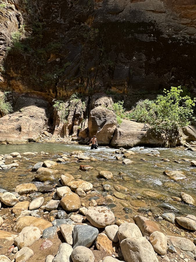 adolescent marchant dans le lit de la Virgin river, de l'eau jusqu'à la taille entre les parois du canyon, lors de la randonnée The Narrows à Zion National Park, Ouest américain