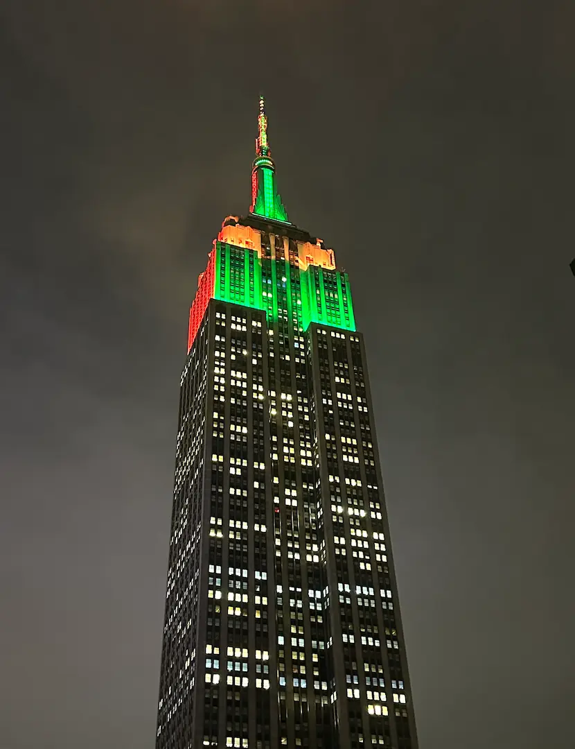 Photo de L'Empire State Building illuminé en orange et vert, prise depuis le bas de l'Empire State Building, de nuit à New York