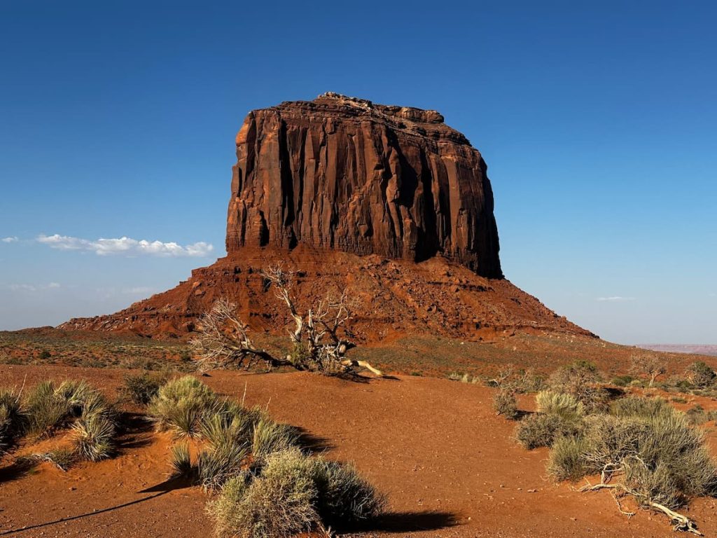 Merrick Butte sur fond de ciel bleu avec le sable et la végétation aride au premier plan à Monument Valley