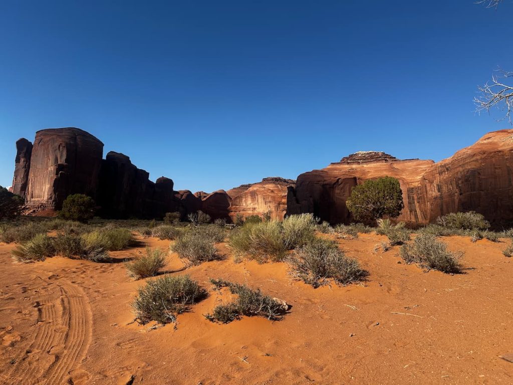 Photo prise dans la Valley de Monument Valley avec des formations rocheuses au coucher du soleil, le sable ocre et la végétation aride