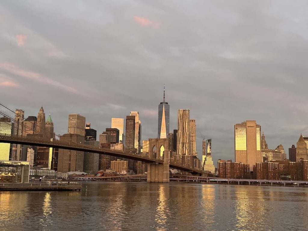 Photo des buildings de Manhattan, prise depuis Brooklyn Park à Dumbo, au lever du soleil avec le ciel rose et les gratte-ciels de couleur doré, à New York