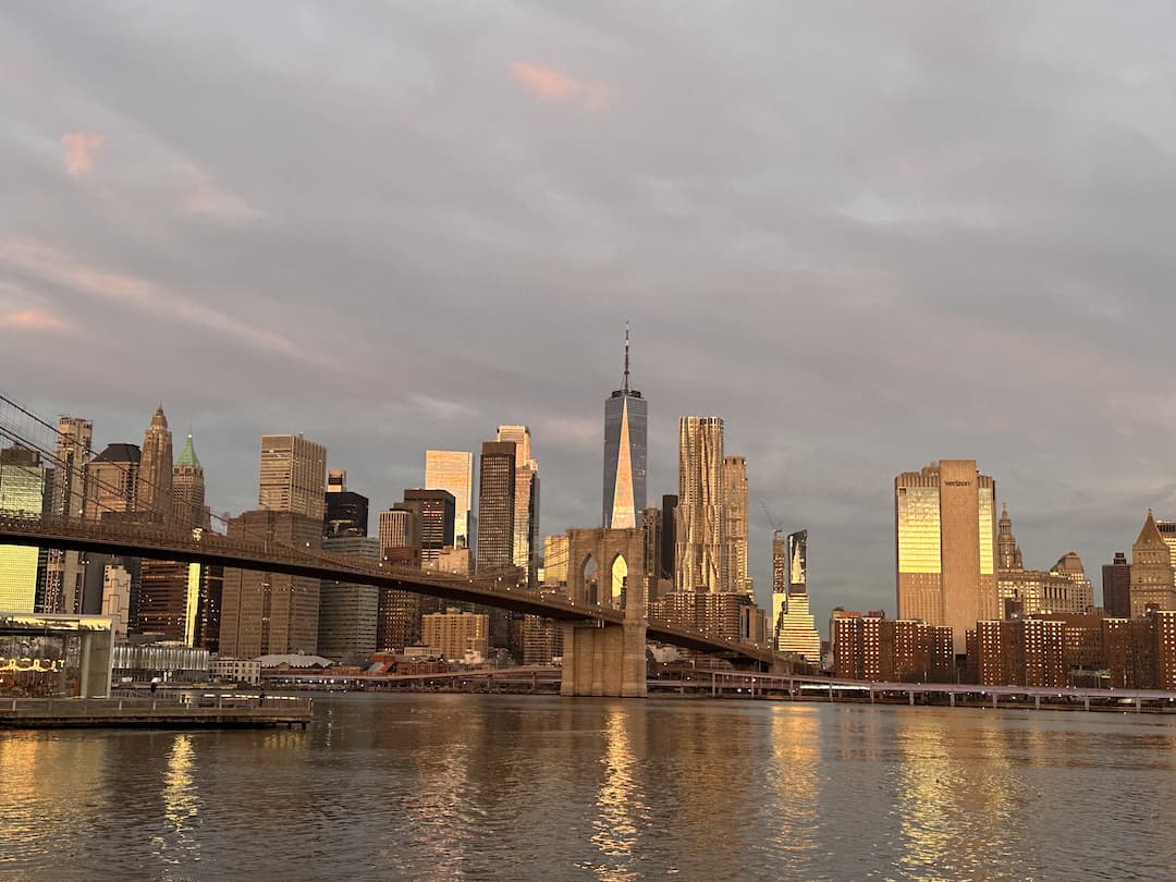 Photo des buildings de Manhattan, prise depuis Brooklyn Park à Dumbo, au lever du soleil avec le ciel rose et les gratte-ciels de couleur doré, à New York