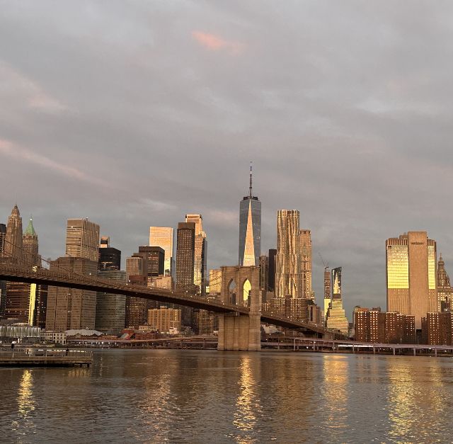 Photo des buldings au lever du soleil, prise sous le pont de Brooklyn, avec la lumière doré se reflétant, à New York
