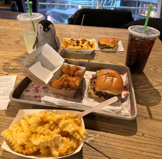 Photo d'une table avec des burgers et des frites, à côté de deux verres de sodas, au Shake Shack à New York