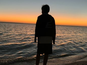 adolescent de dos, face à l'océan, au coucher du soleil à Holbox au Mexique