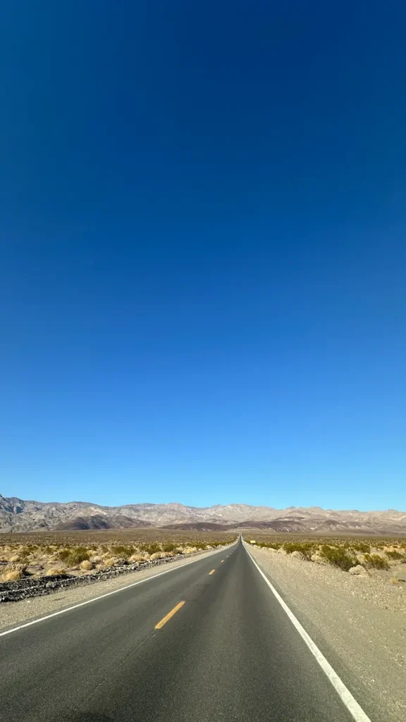 Photo d'une route goudronée à perte de vue à Death Valley avec les montagnes en fond et le ciel bleu