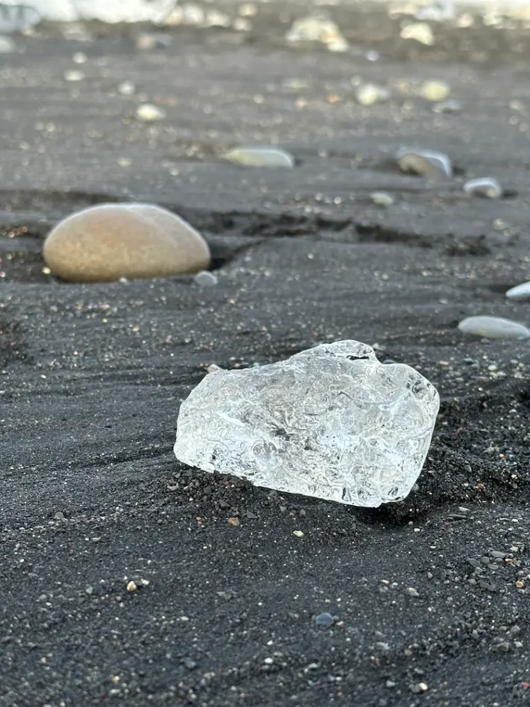 Pierre ronde polie et morceau d'iceberg scintillant sur le sable noir de la plage de diamond Beach, près de la lagune glacière de Jökulsárlón dans le sud de l'Islande