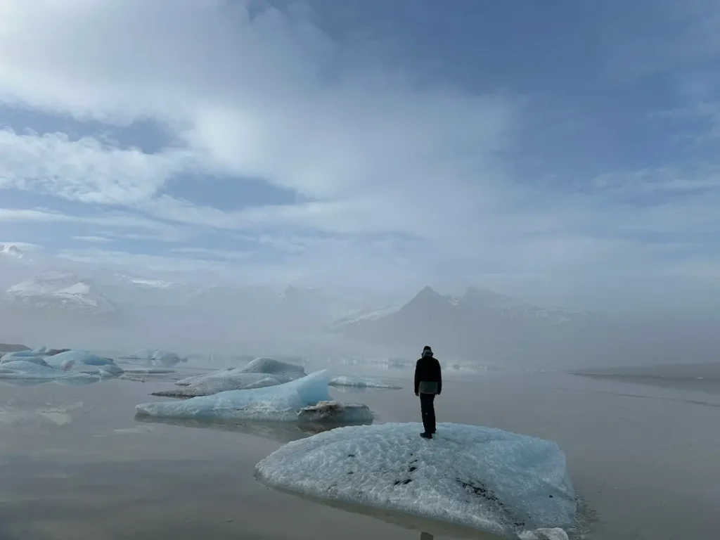 Adolescent de dos, debout sur un iceberg, dans la lagune glacière de Fjallsárlón en Islande