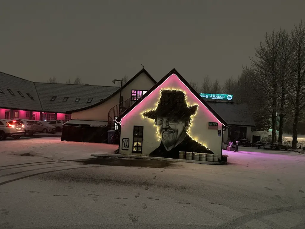 Façade de l'hotel Laxnes, de nuit avec le portrait en street art et les néons roses, le parking enneigé, à Mosfellsbaer en Islande