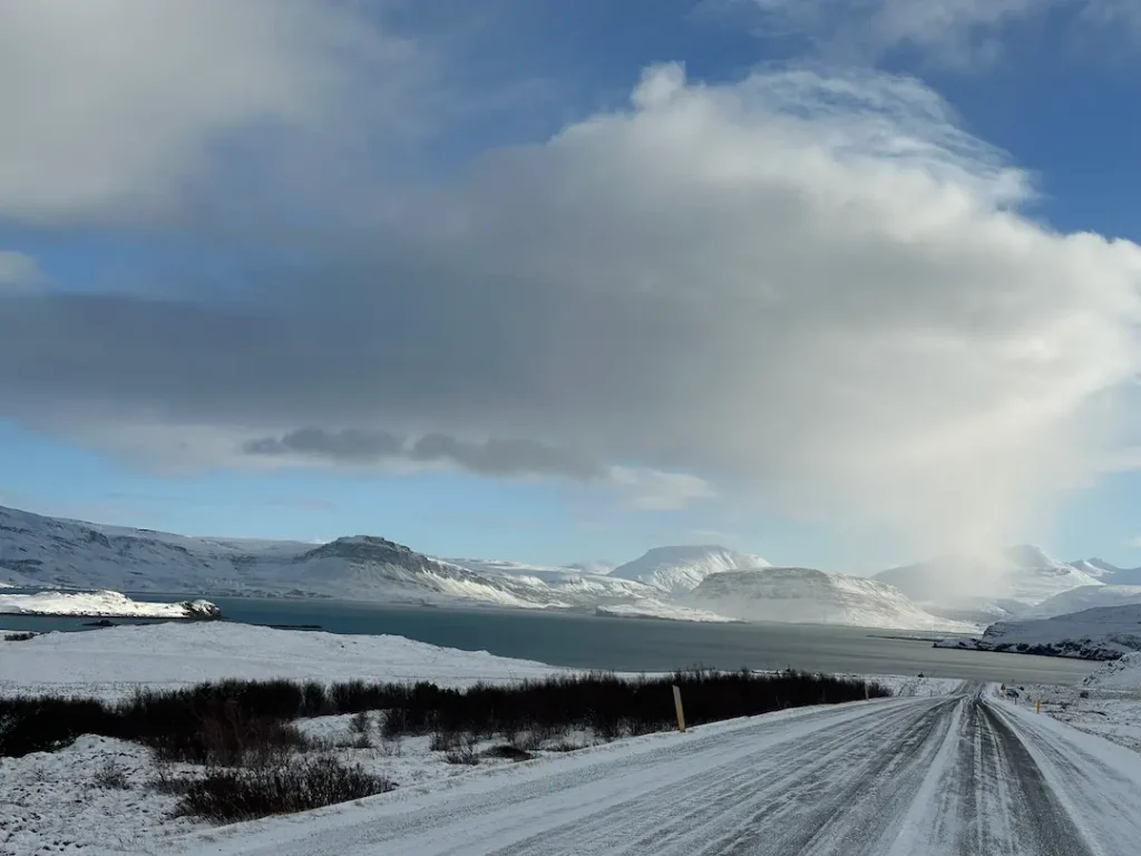 Photo d'une route enneigée avec vue sur fjord, prise depuis l'intérieur d'une voiture, en Islande