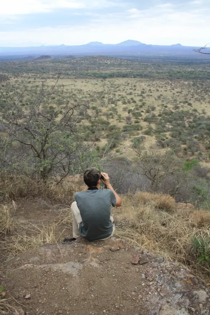 Adolescent assis, de dos, avec des jumelles pour observer la savane au Parc National de Tsavo Ouest, Kenya