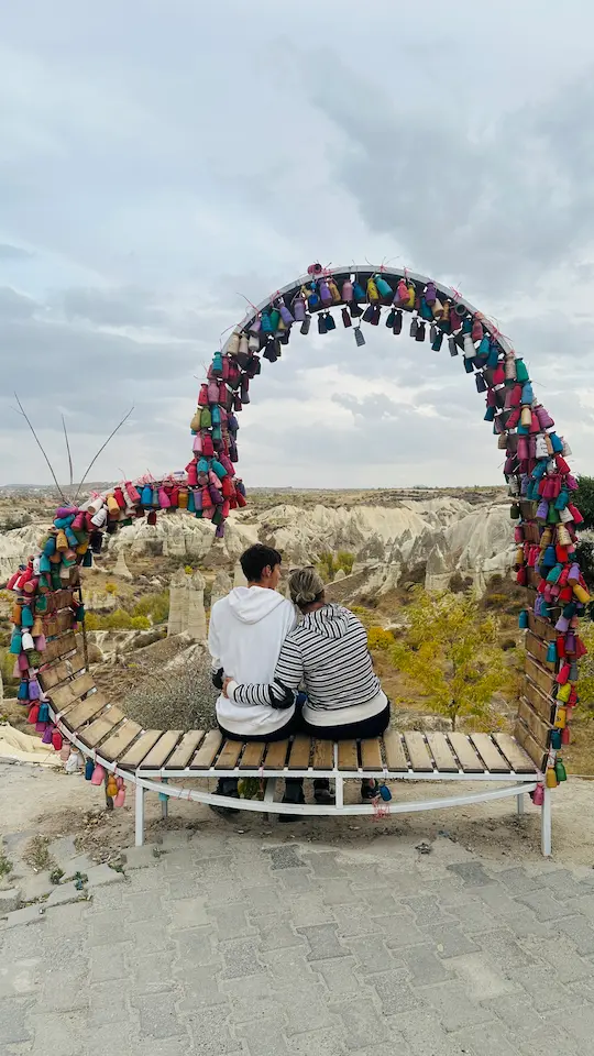 Un ado et sa mère, assis sur un banc entouré par un cœur, bras dessus, bras dessous, à Love Valley, Goreme, Cappadoce, Turquie