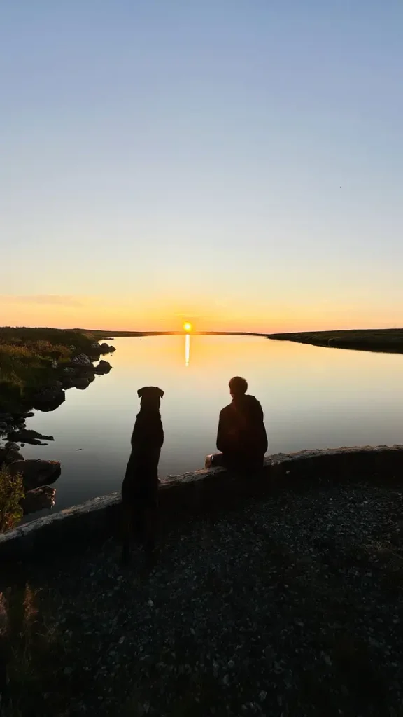 Adolescent et chien de dos au coucher du soleil devant un loch, Ecosse, Royaume Uni