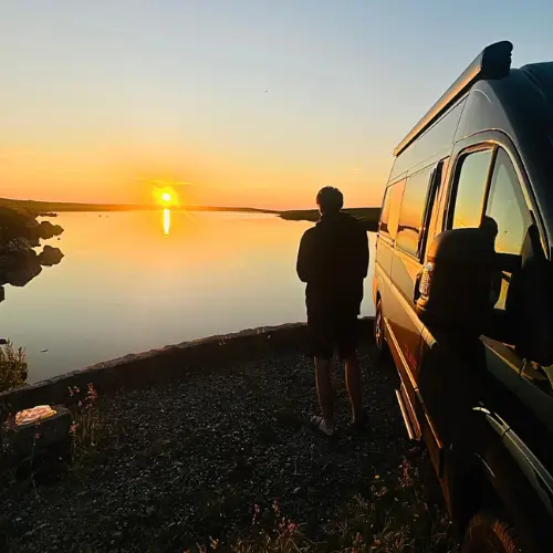 ado a cote du van amenage au coucher du soleil devant un loc en ecosse Adolescent à côté d'un van aménagé, au coucher du soleil, devant un loch, sur l'ile de Lewis dans les Hébrides extérieures, Ecosse, Royaume Uni